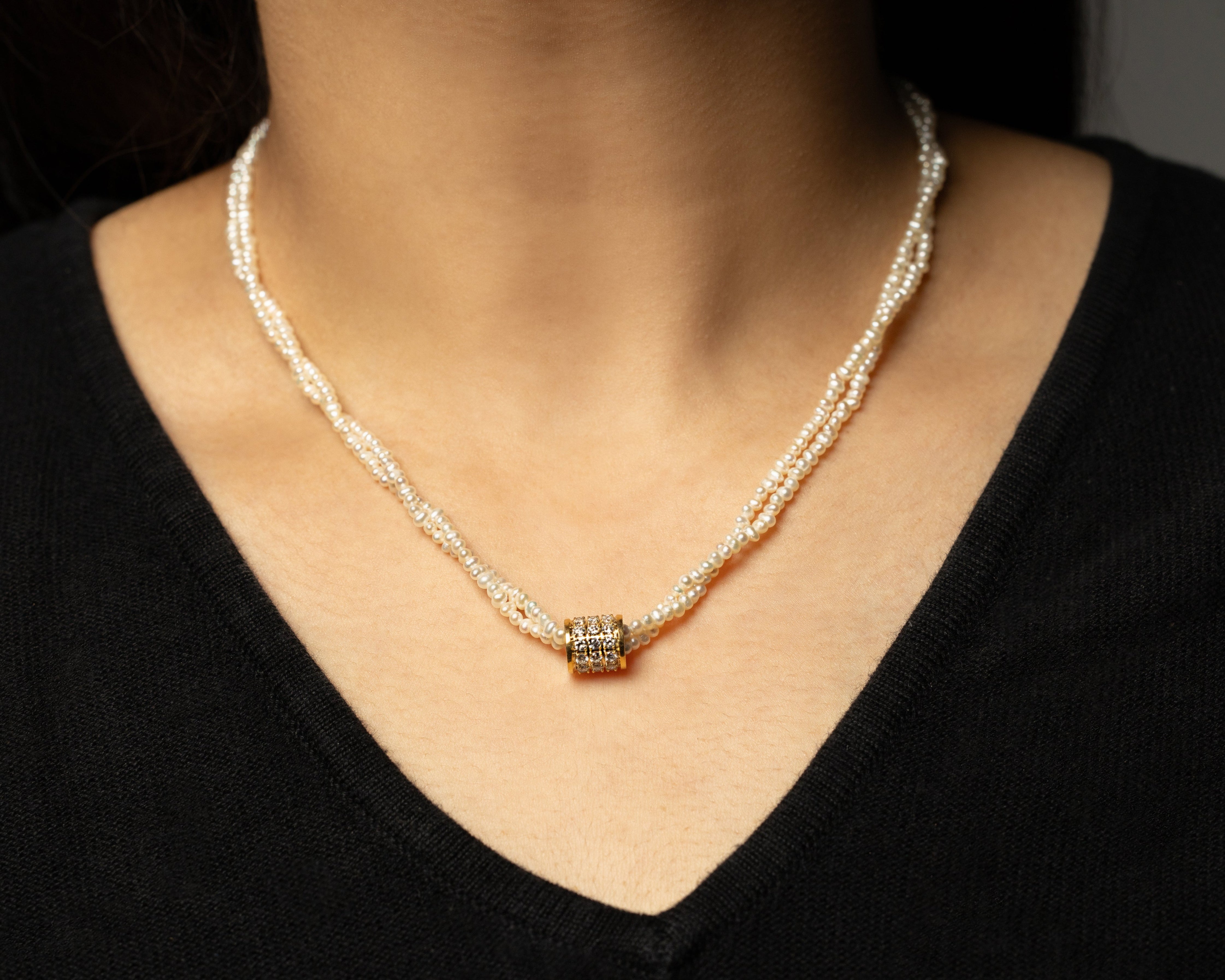 Pearl necklace with a gold clasp worn by a person against a dark background