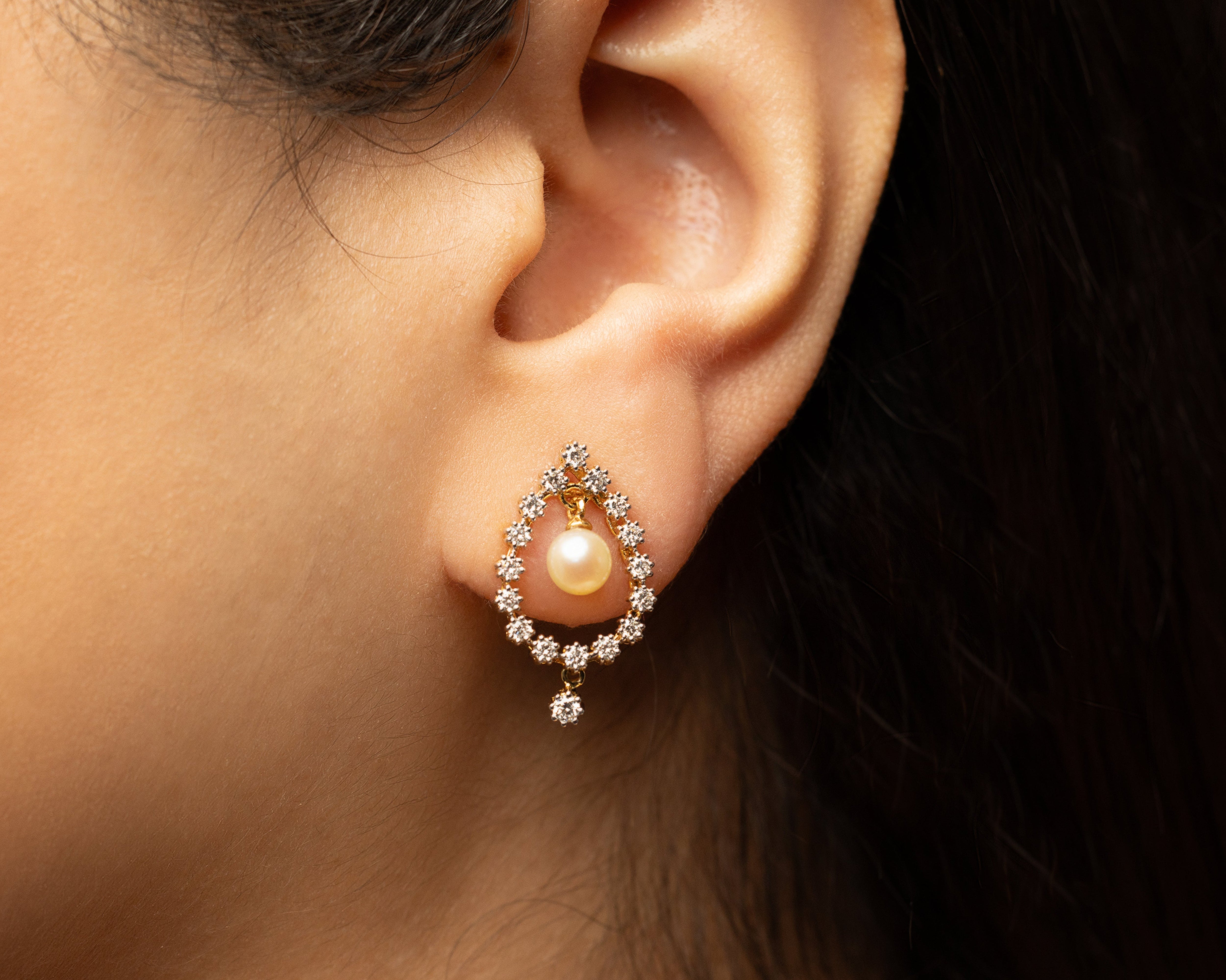 Close-up of an ear wearing a pearl earring with lab grown diamonds with a blurred background