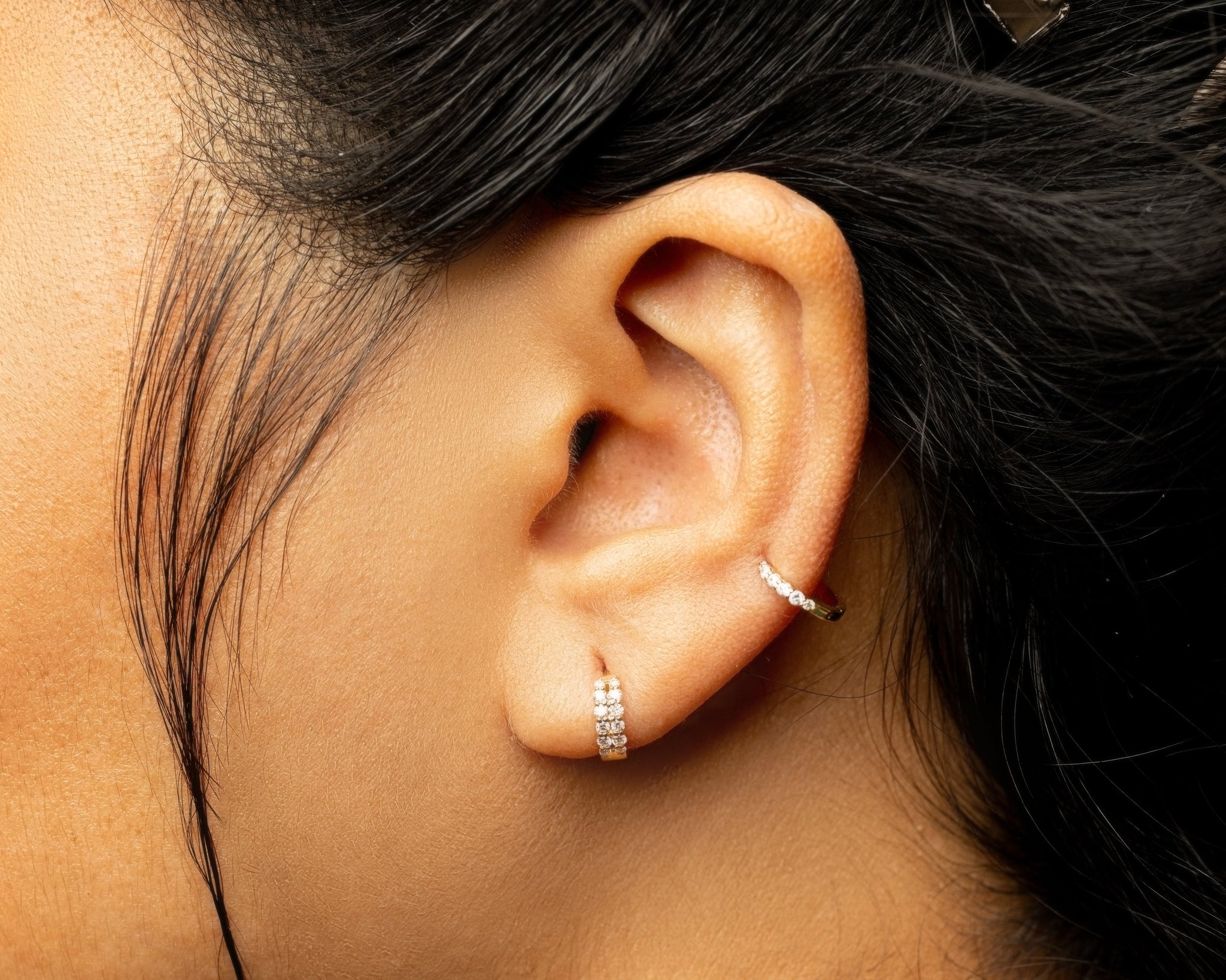 Close-up of a person's ear with diamond hoop earrings on primary and secondary piercings