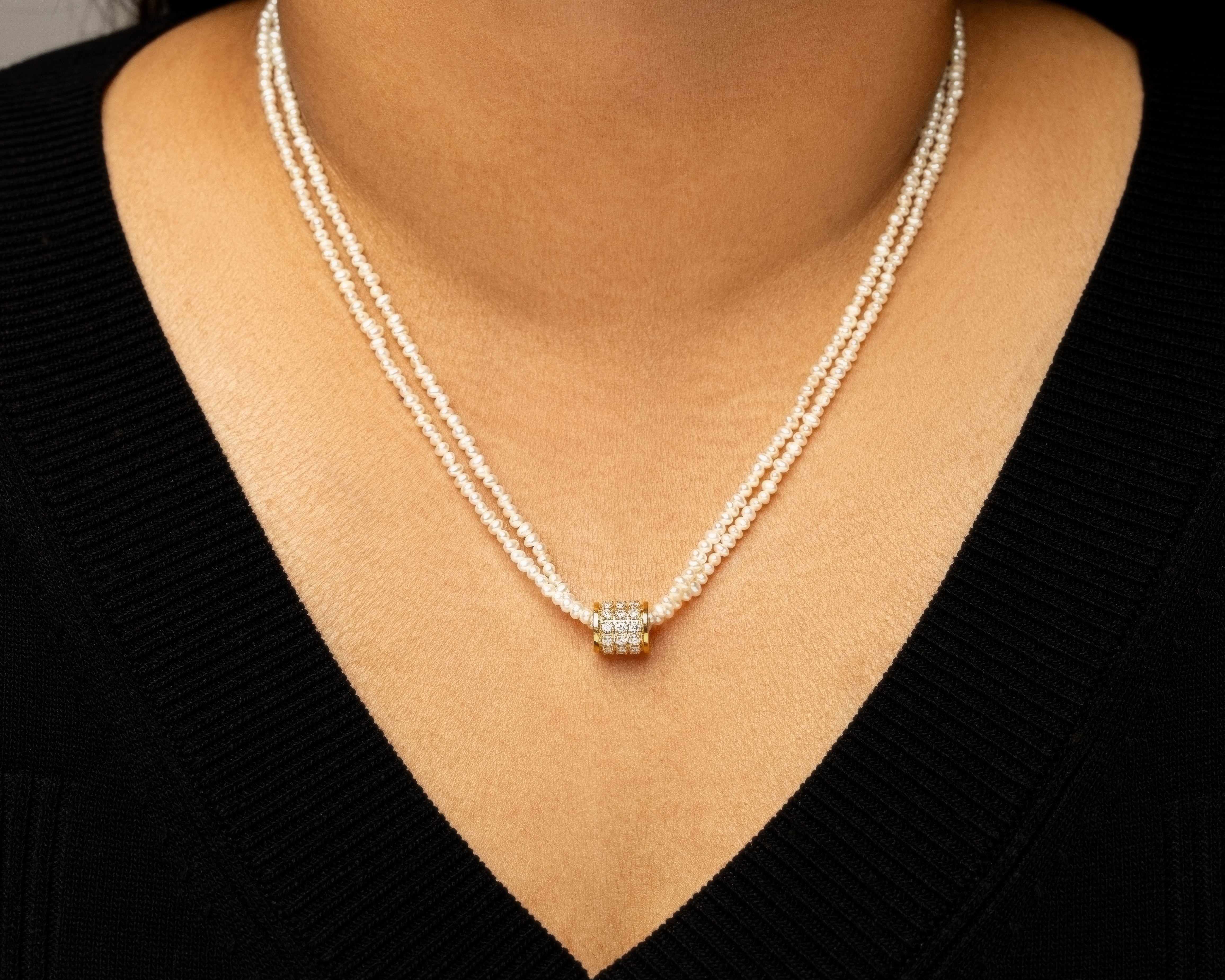 Pearl necklace with a diamond pendant worn by a person in a black top.