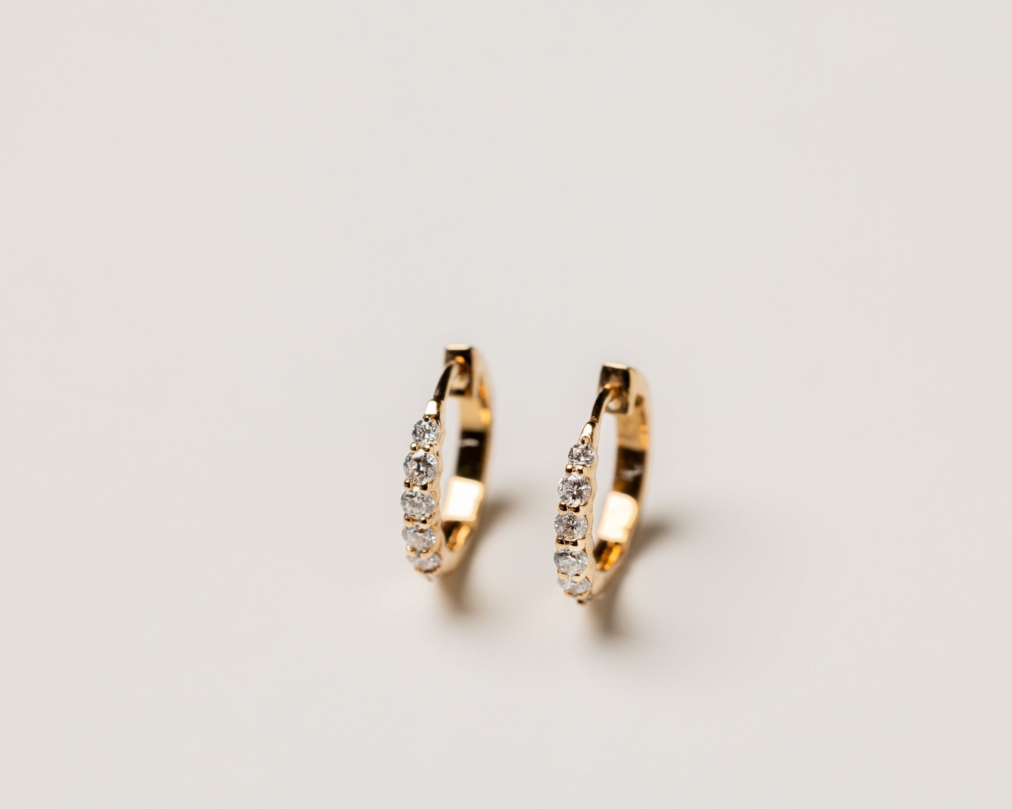 Gold hoop earrings studded with diamonds on a light gray background
