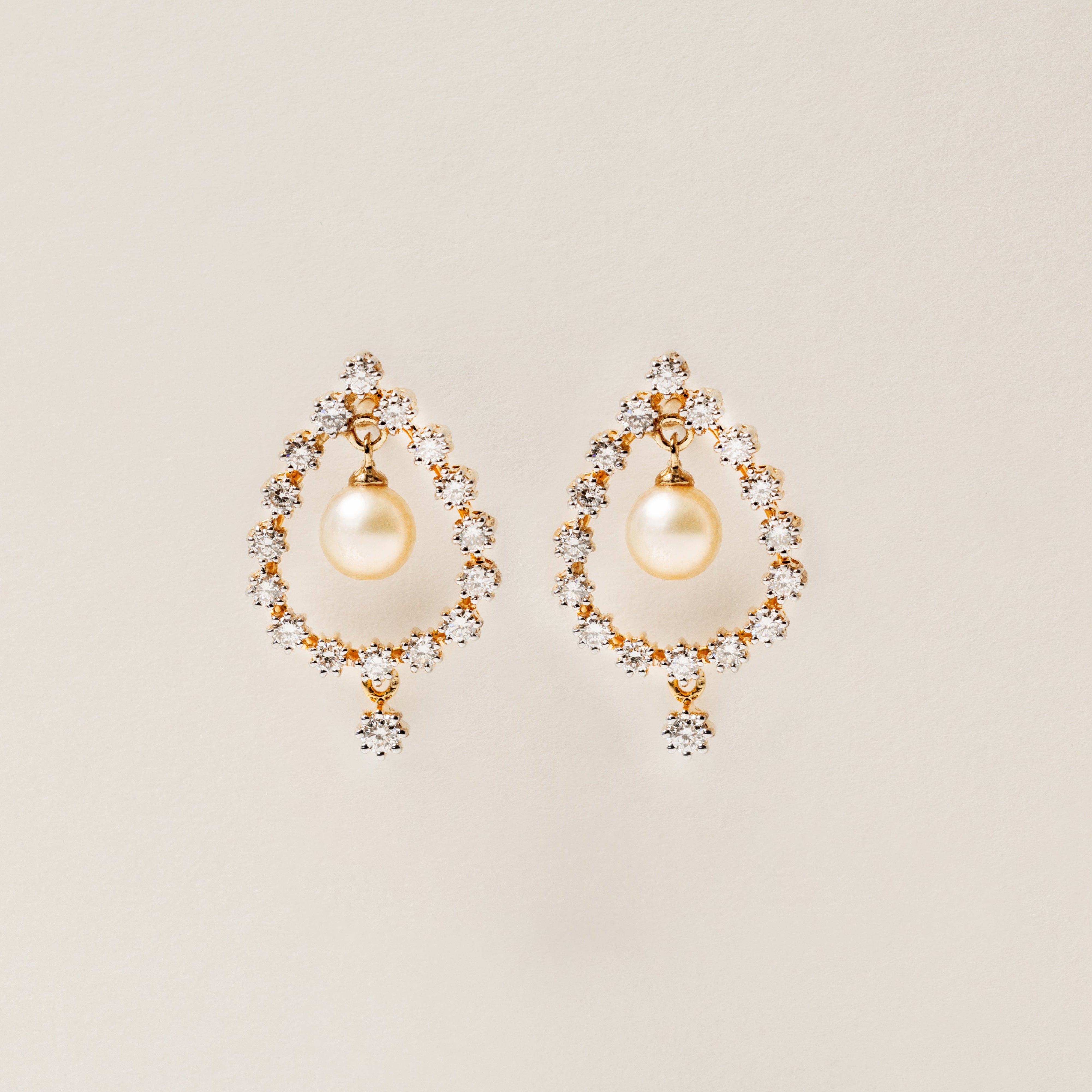 Pair of pearl earrings with gold accents on a beige background