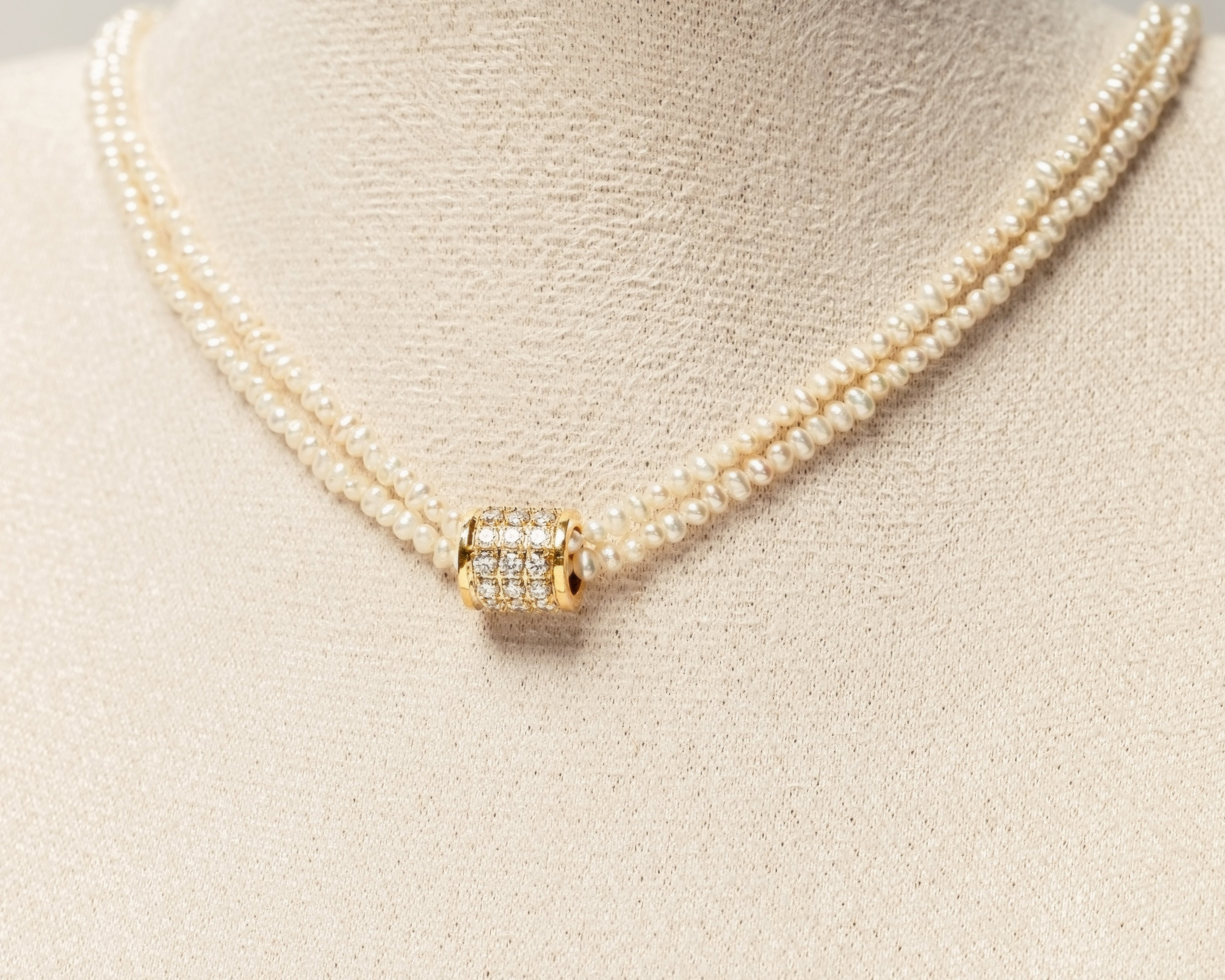 Pearl necklace with a gold clasp studded with diamonds on a mannequin bust.