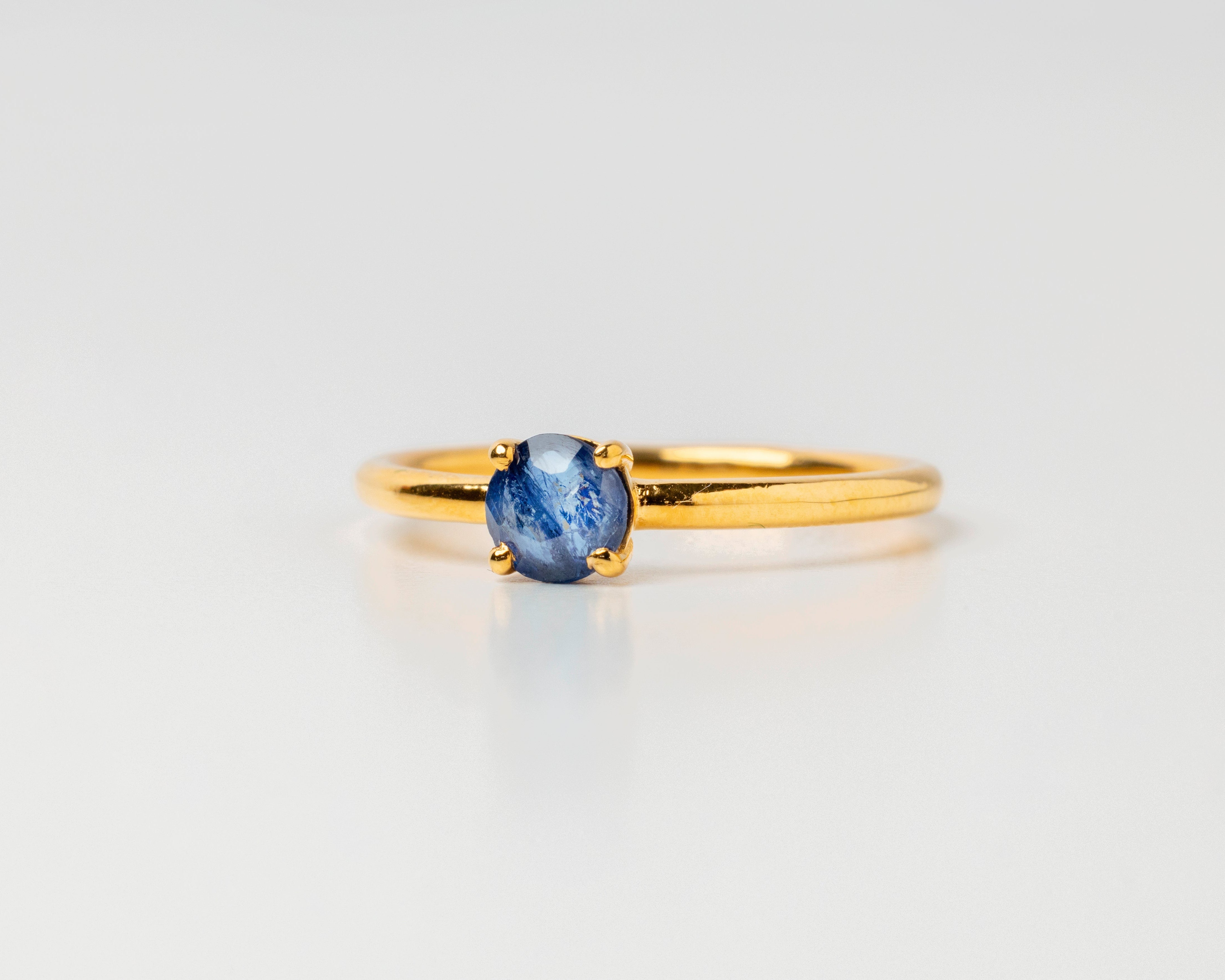 Gold ring with a blue sapphire gemstone on a light gray background