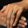Close-up of a hand wearing an emerald and diamond ring against a blurred background