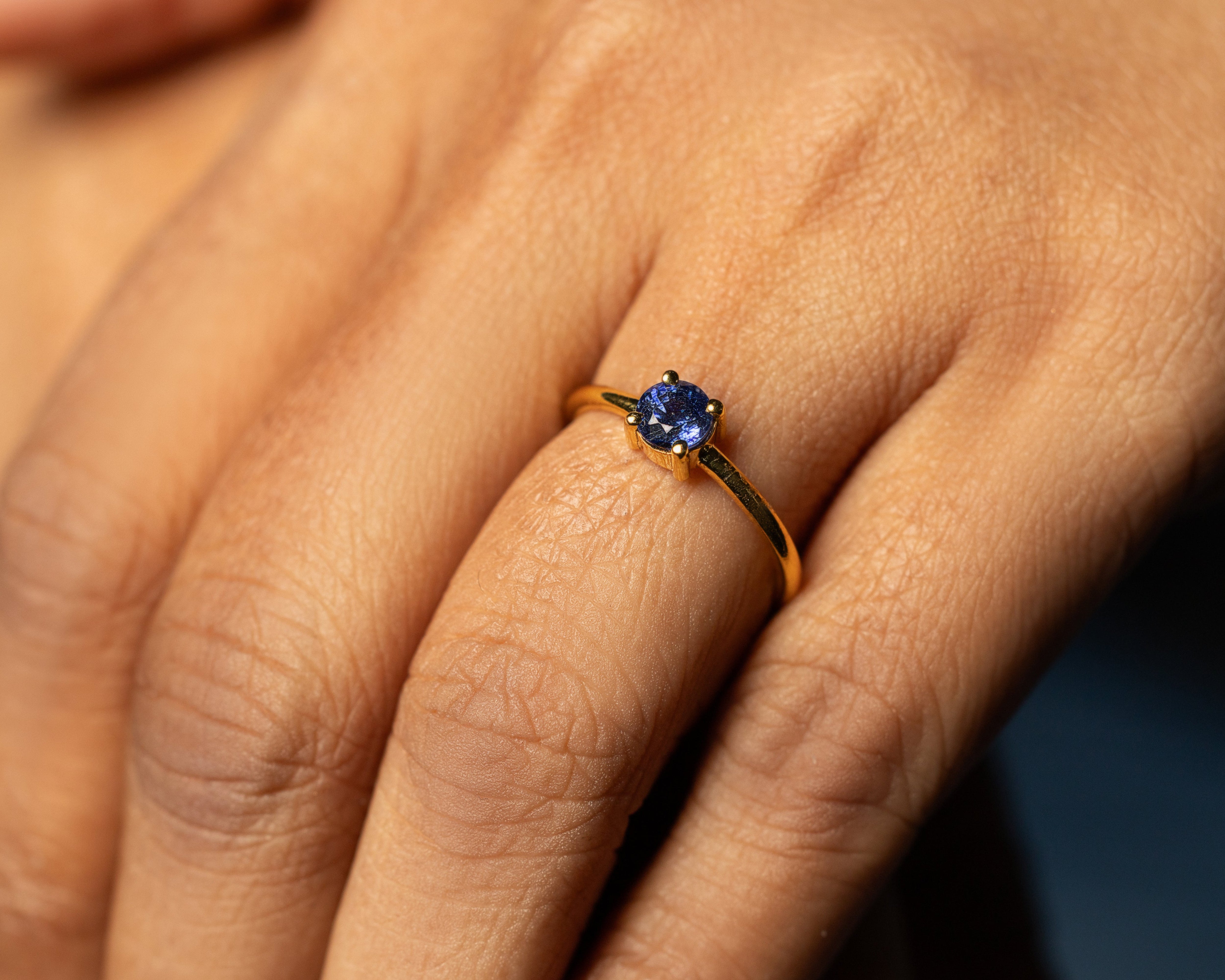 Close-up of a hand wearing a gold ring with a blue gemstone on a dark background
