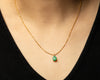 Person wearing delicate solid gold necklace with a green emerald pear shaped pendant with a black top