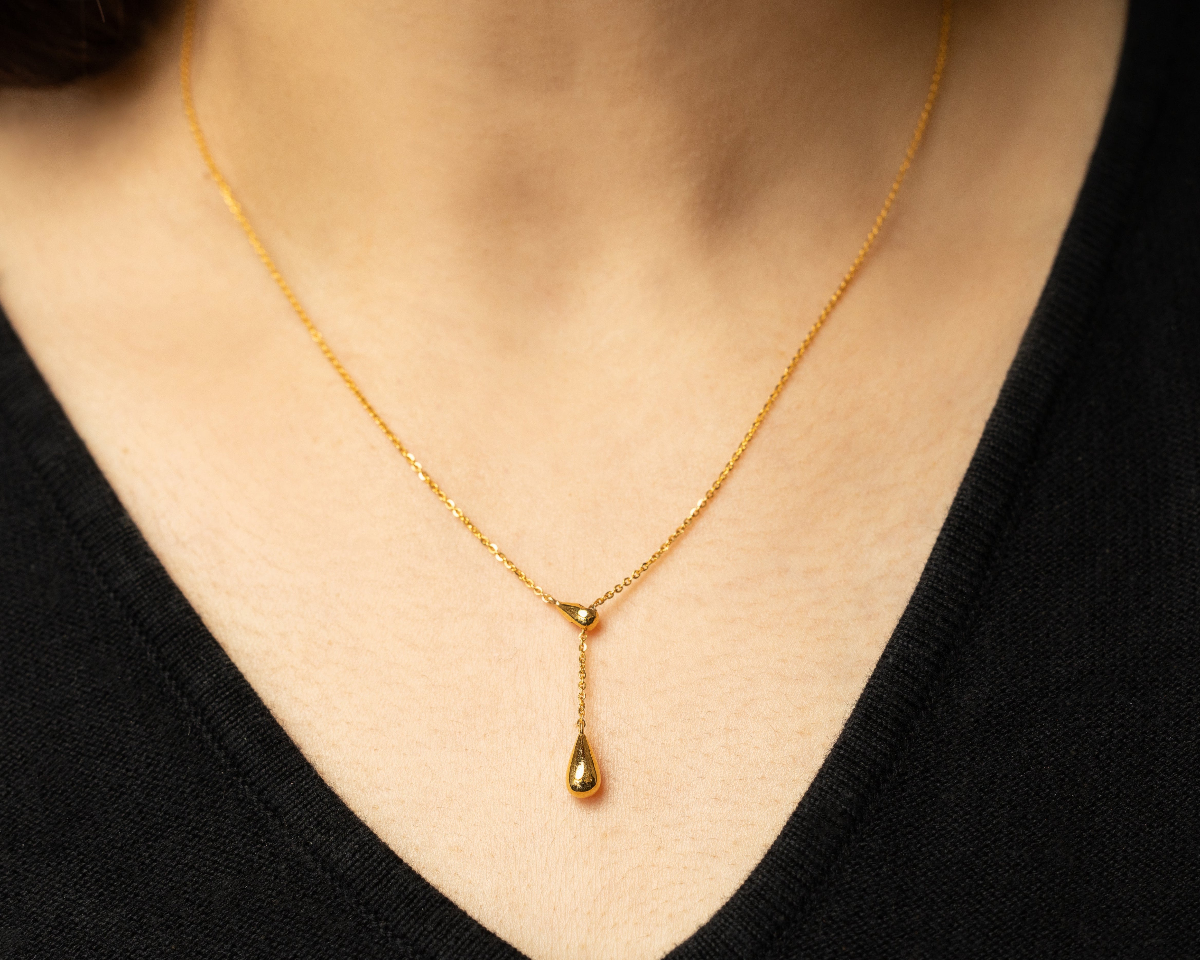 Gold necklace with a teardrop pendant worn by a person with a black top