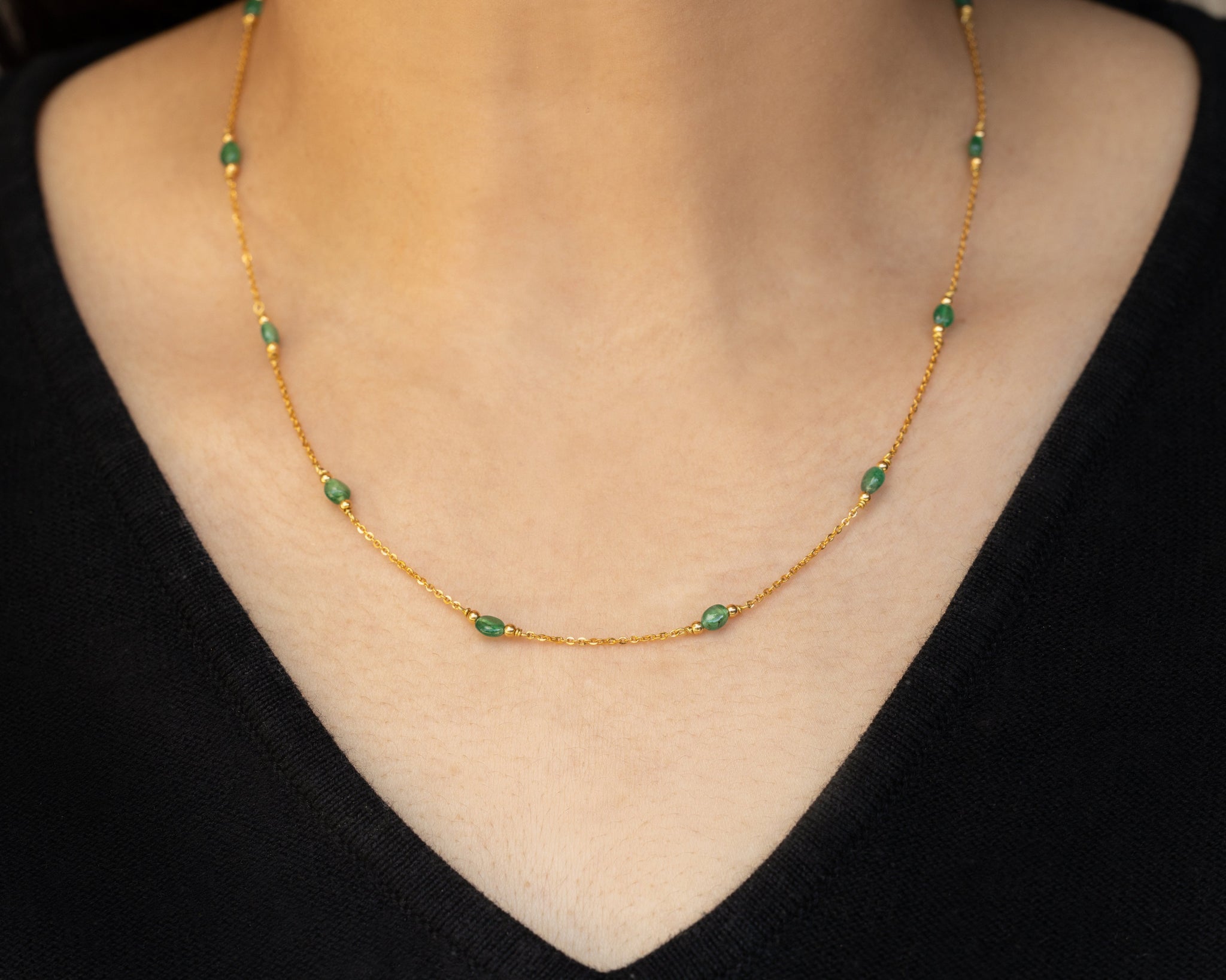 Solid gold necklace with green beads worn by a person against a black background