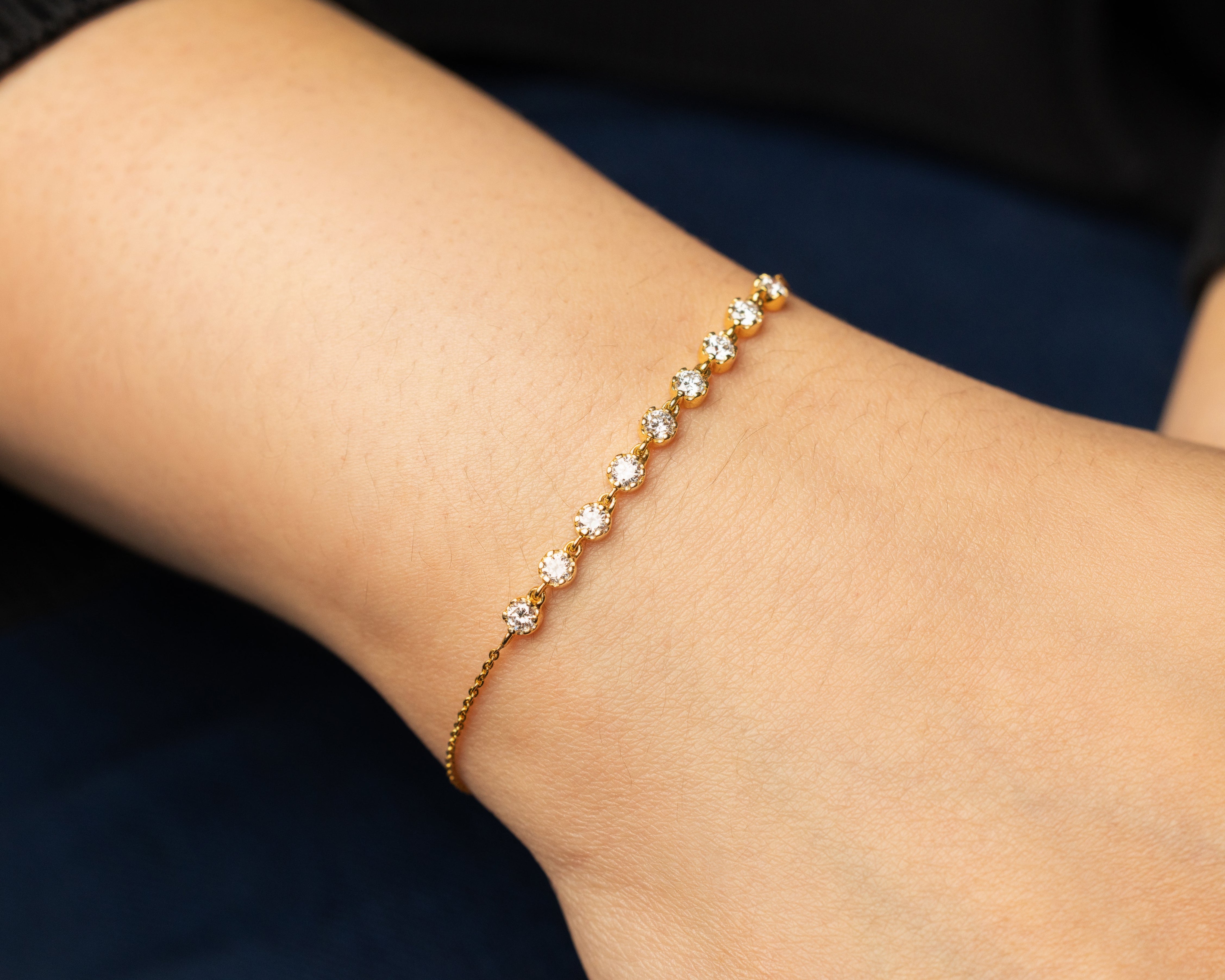 Delicate solid gold bracelet with sparkling diamonds on a wrist against a dark background