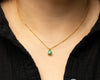 Delicate solid gold necklace with a green emerald pendant worn by a person in a black shirt.