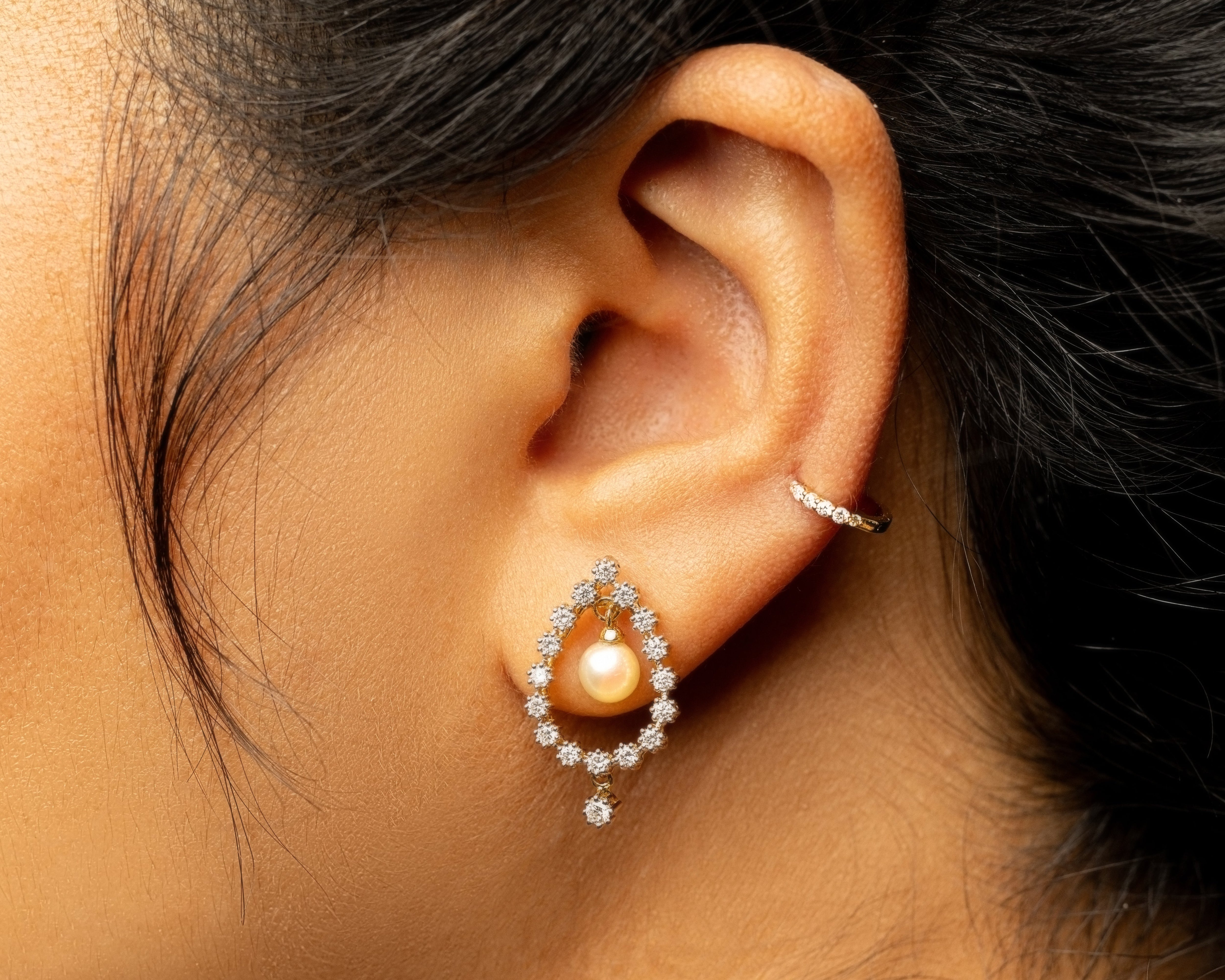 Close-up of an ear wearing a gold earring with a diamond stone.