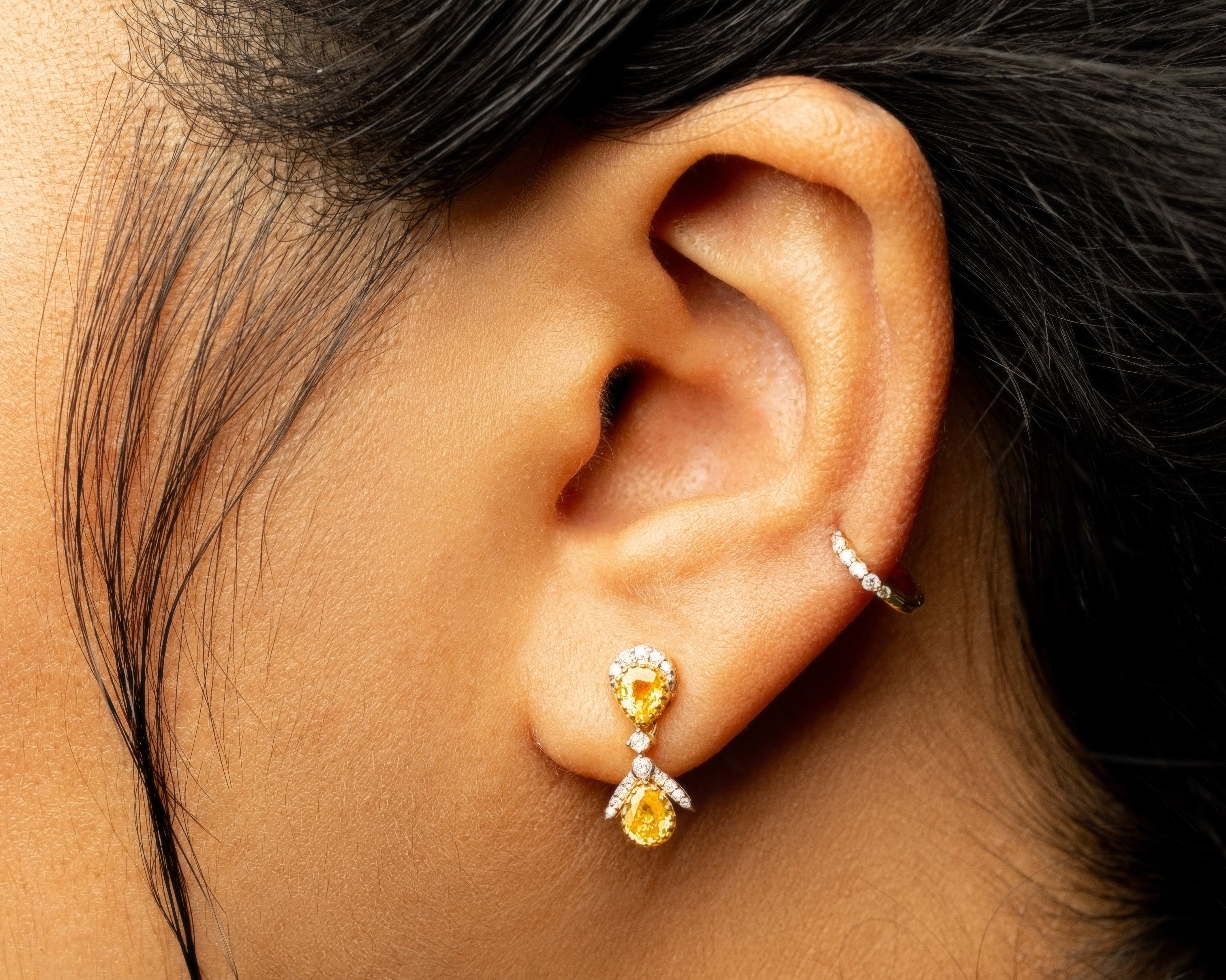 Close-up of an ear wearing a yellow sapphire gemstone earring and a diamond stud.