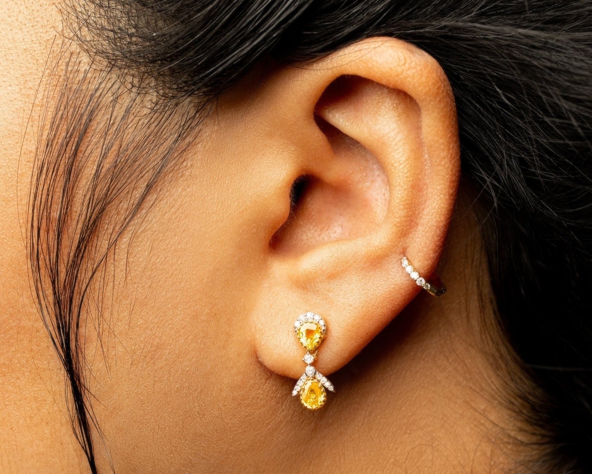 Close-up of an ear wearing a yellow sapphire gemstone earring and a diamond stud.