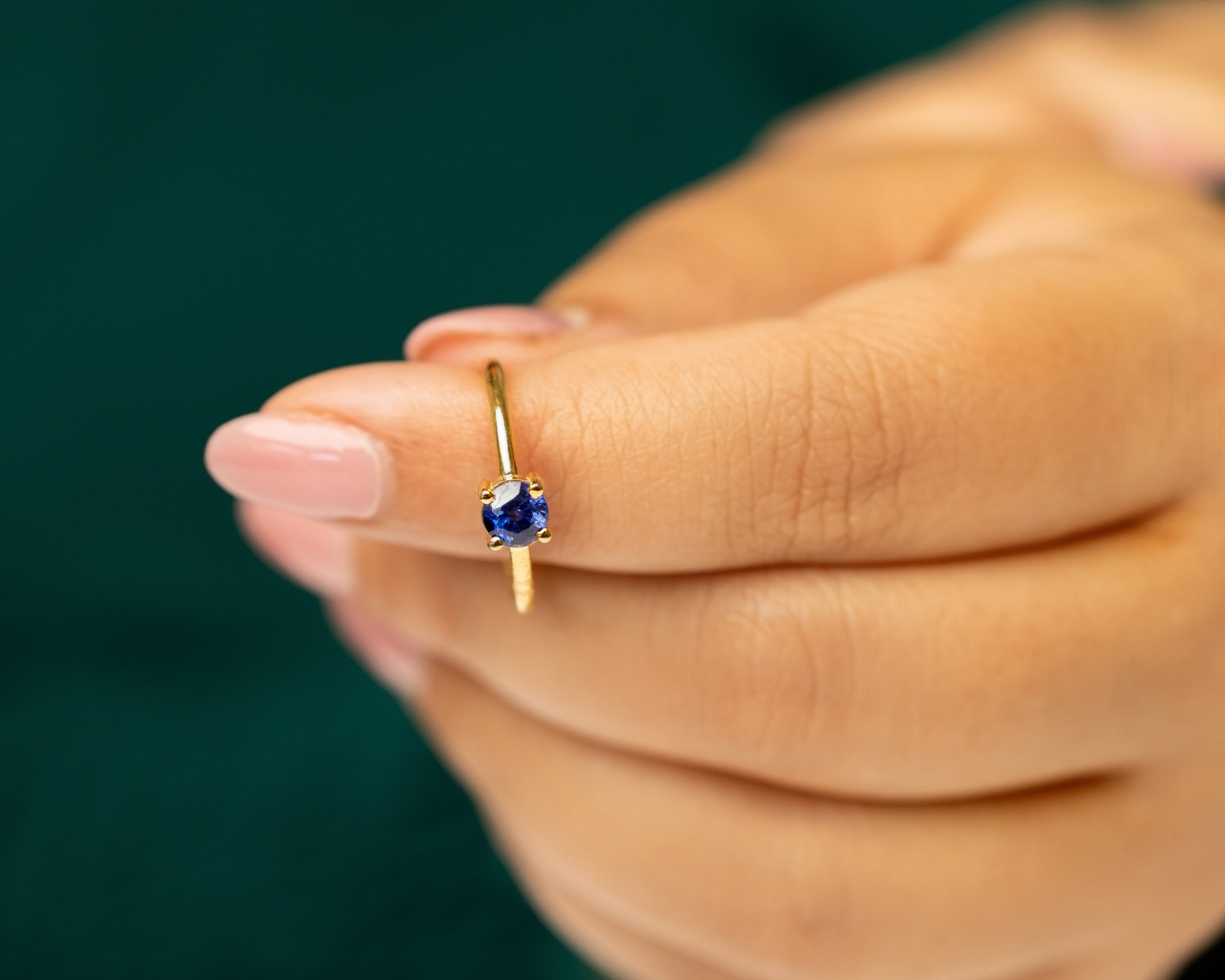 Gold ring with a blue sapphire gemstone worn on a finger against a blurred green background