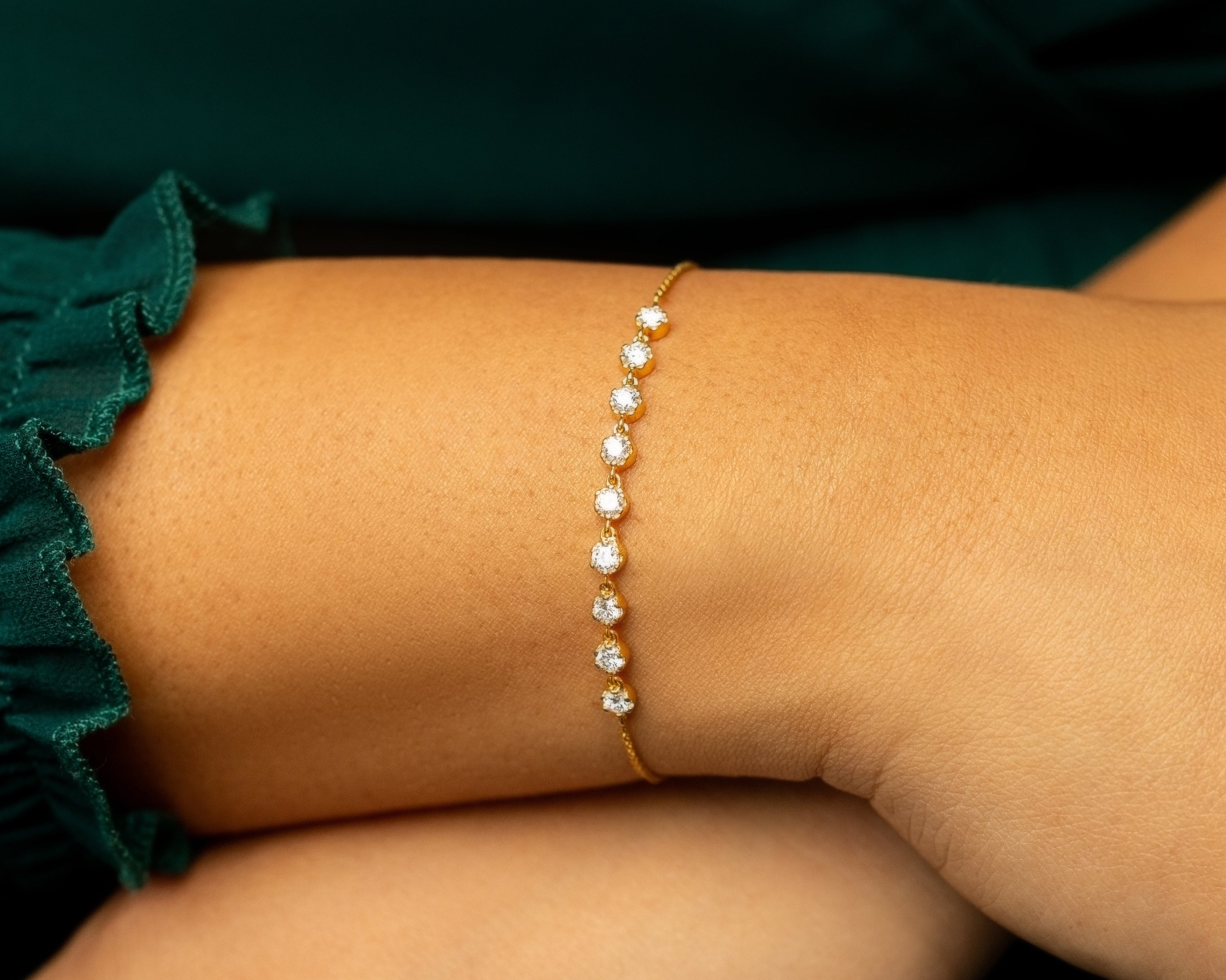 Gold bracelet with adorned with lab grown diamonds on a person's wrist against a green garment.