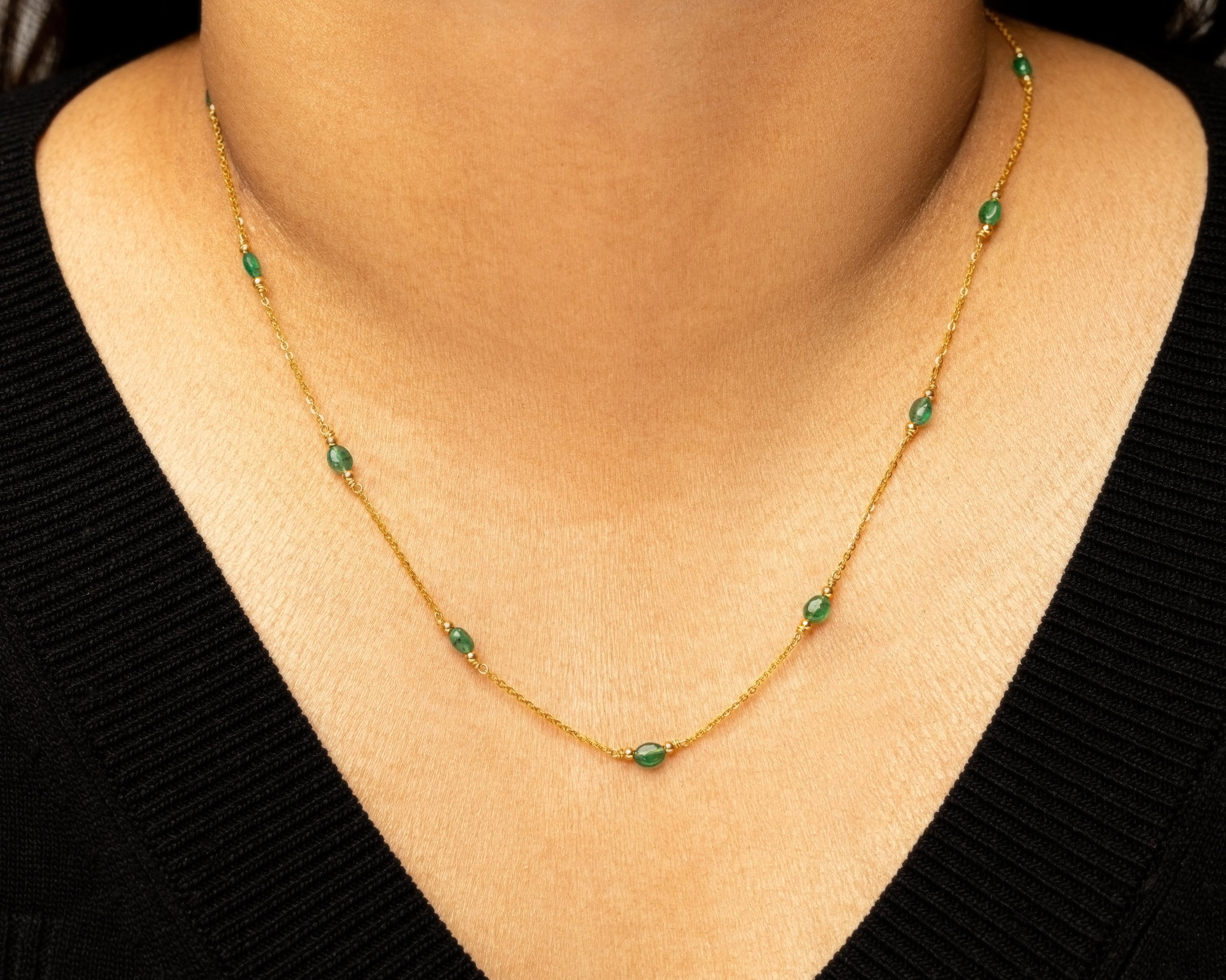 Gold necklace with green beads worn by a person against a black background