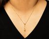 Gold lariat necklace worn by a person against a neutral background