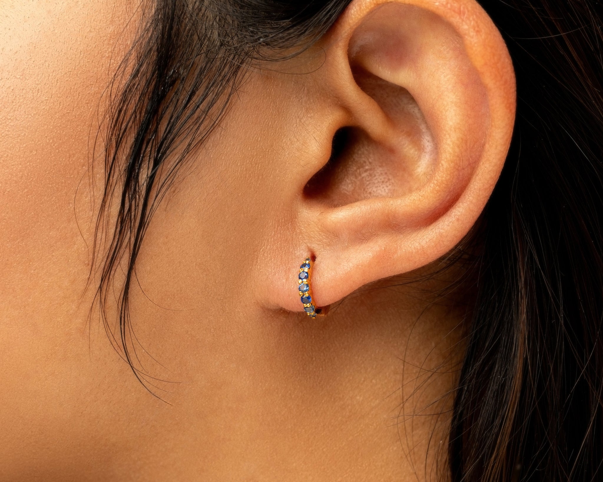 Close-up of an ear wearing a small hoop earring with blue sapphire gemstones.