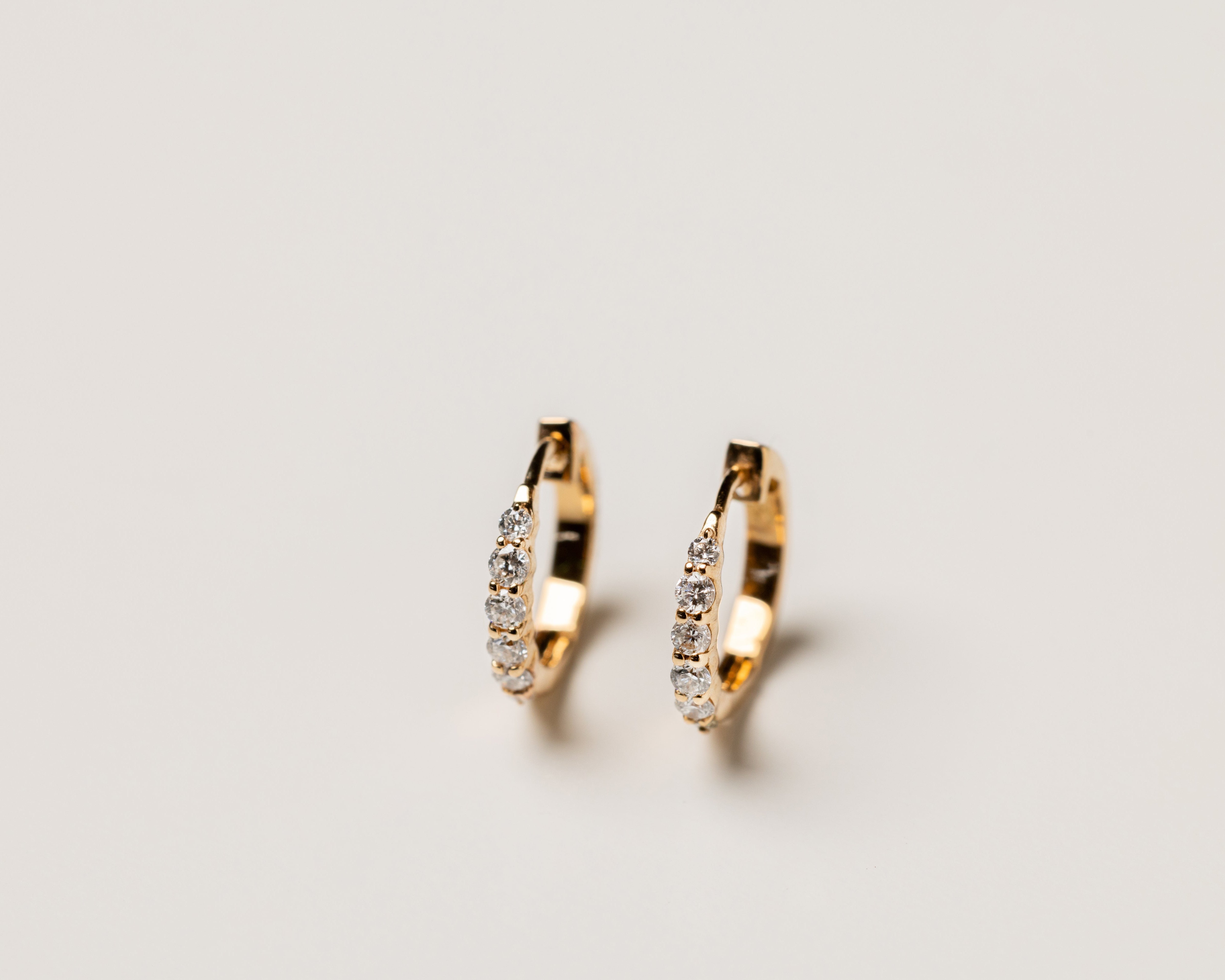 Gold hoop earrings studded with diamonds on a light gray background