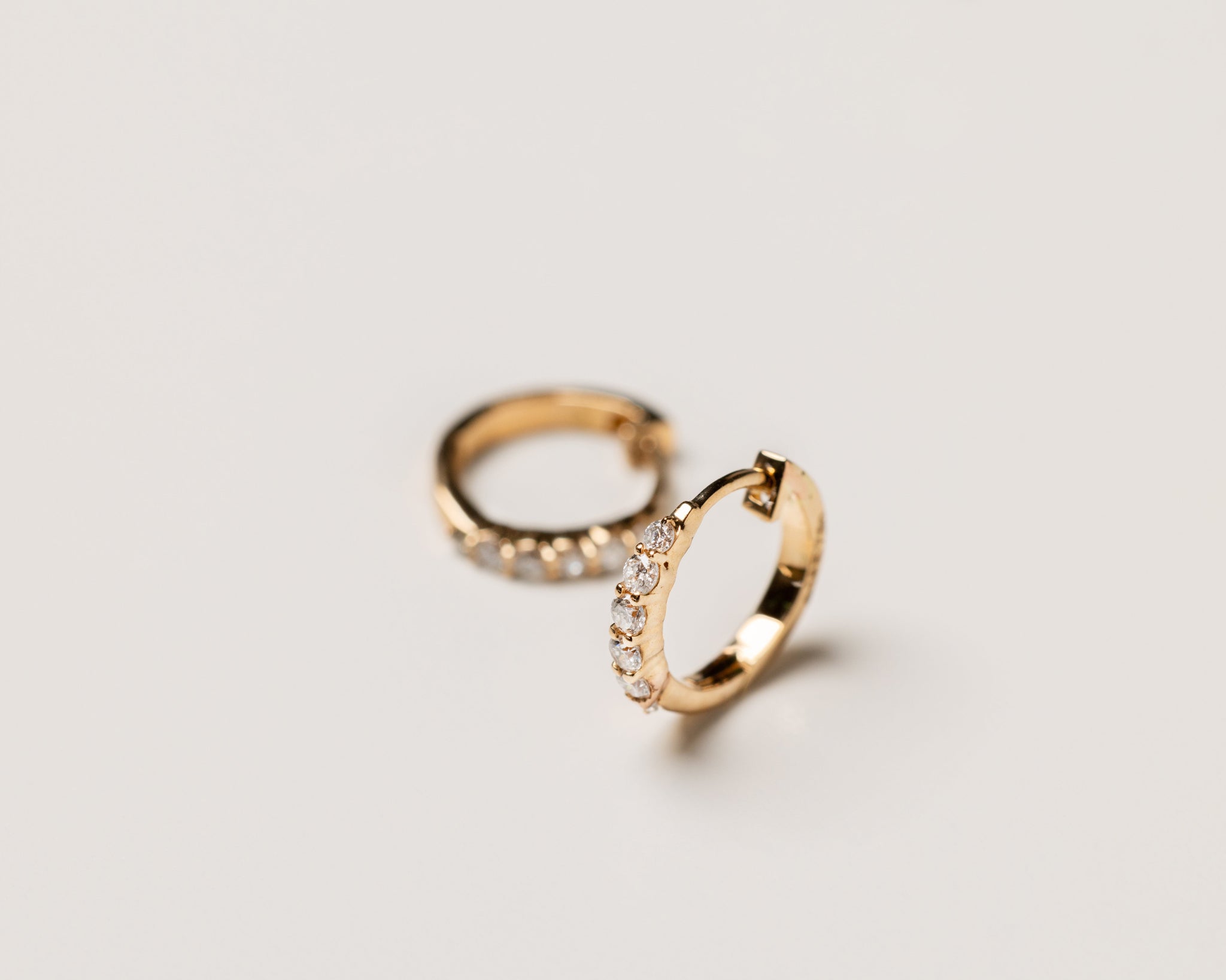 Two 18k solid gold earrings studded with lab grown diamonds on a light gray background