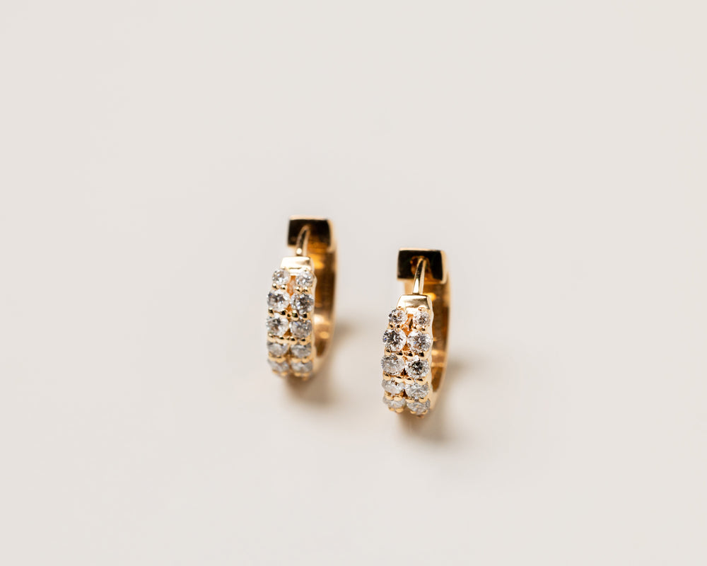 Gold hoop earrings with embedded diamond gemstones on a light beige background