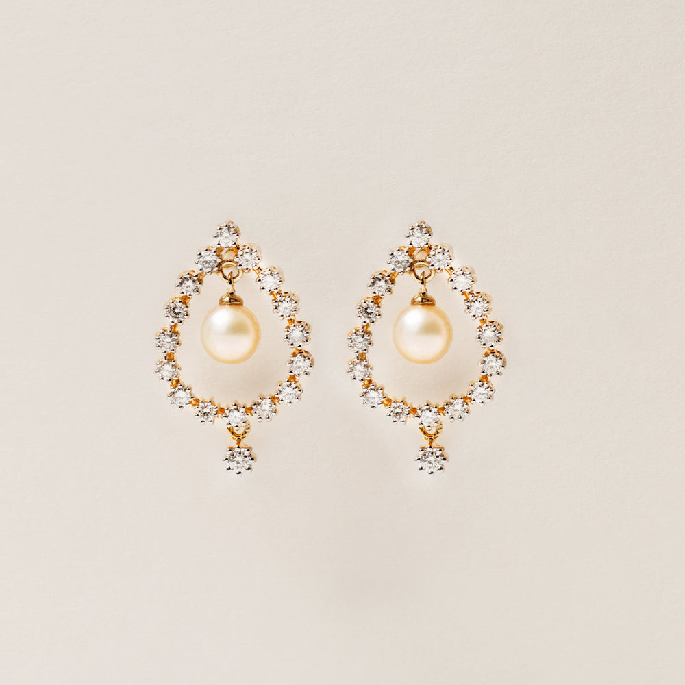 Pair of pearl earrings with gold accents on a beige background