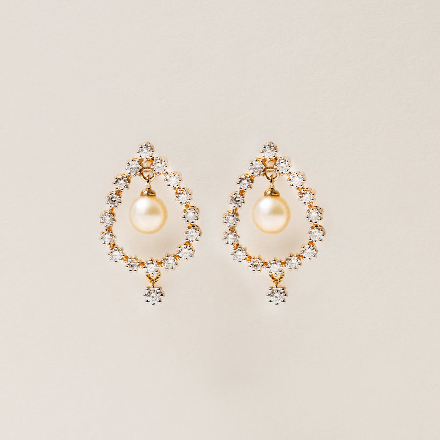Pair of pearl earrings with gold accents on a beige background