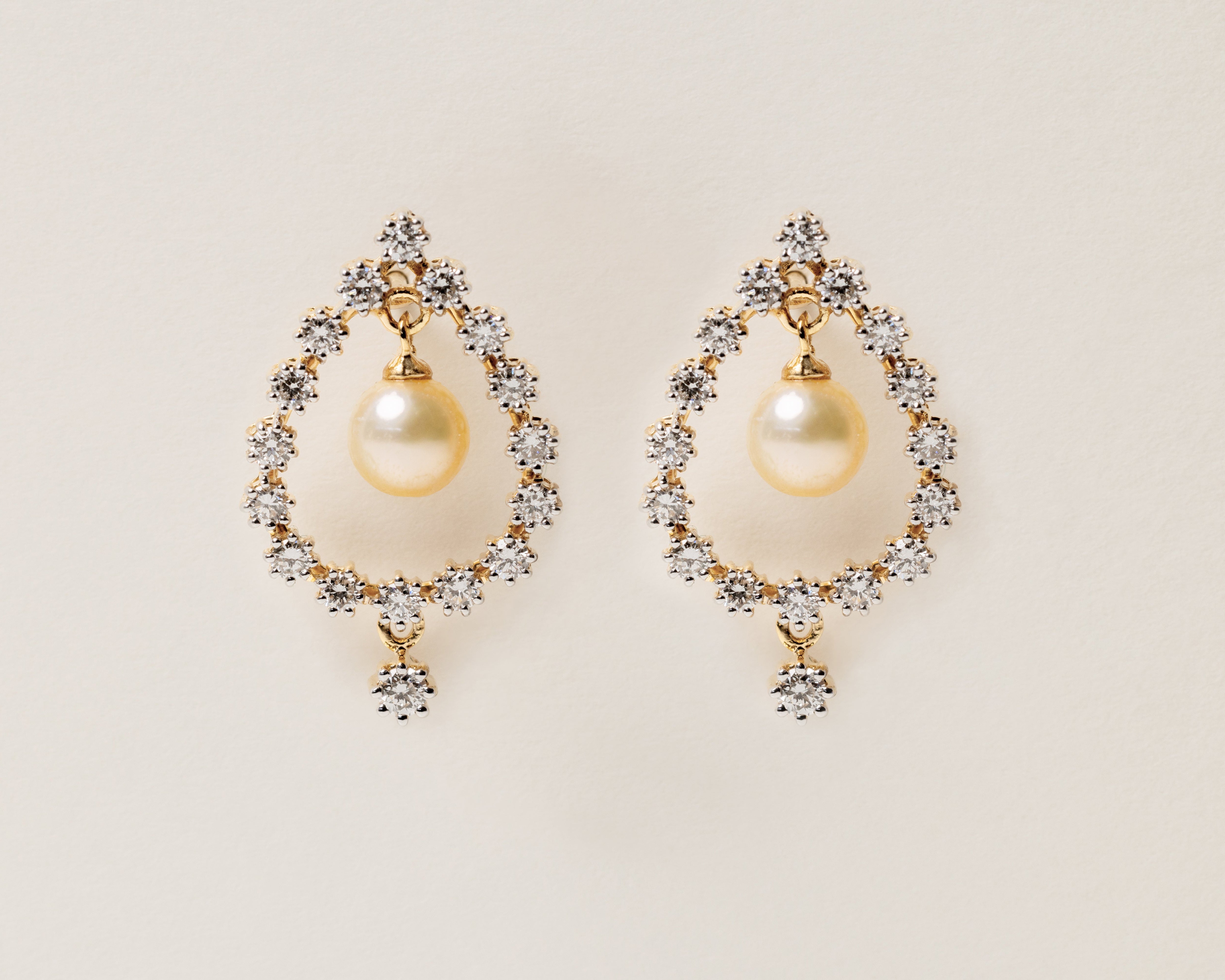 Pair of pearl earrings with gold accents and diamonds on a light beige background