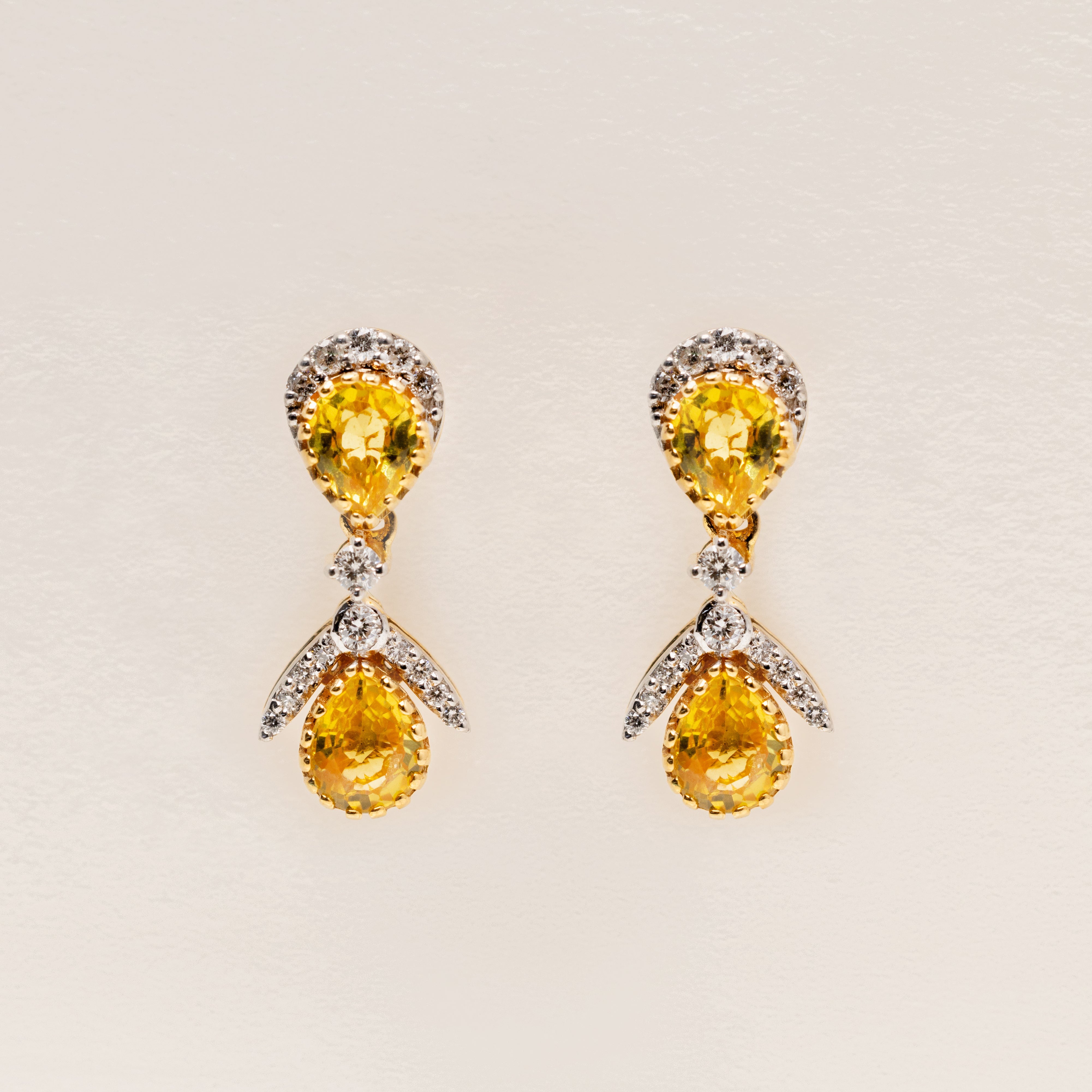 Pair of 18k solid gold earrings with yellow sapphire teardrop gemstone and diamonds on a light beige background