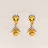 Pair of 18k solid gold earrings with yellow sapphire teardrop gemstone and diamonds on a light beige background