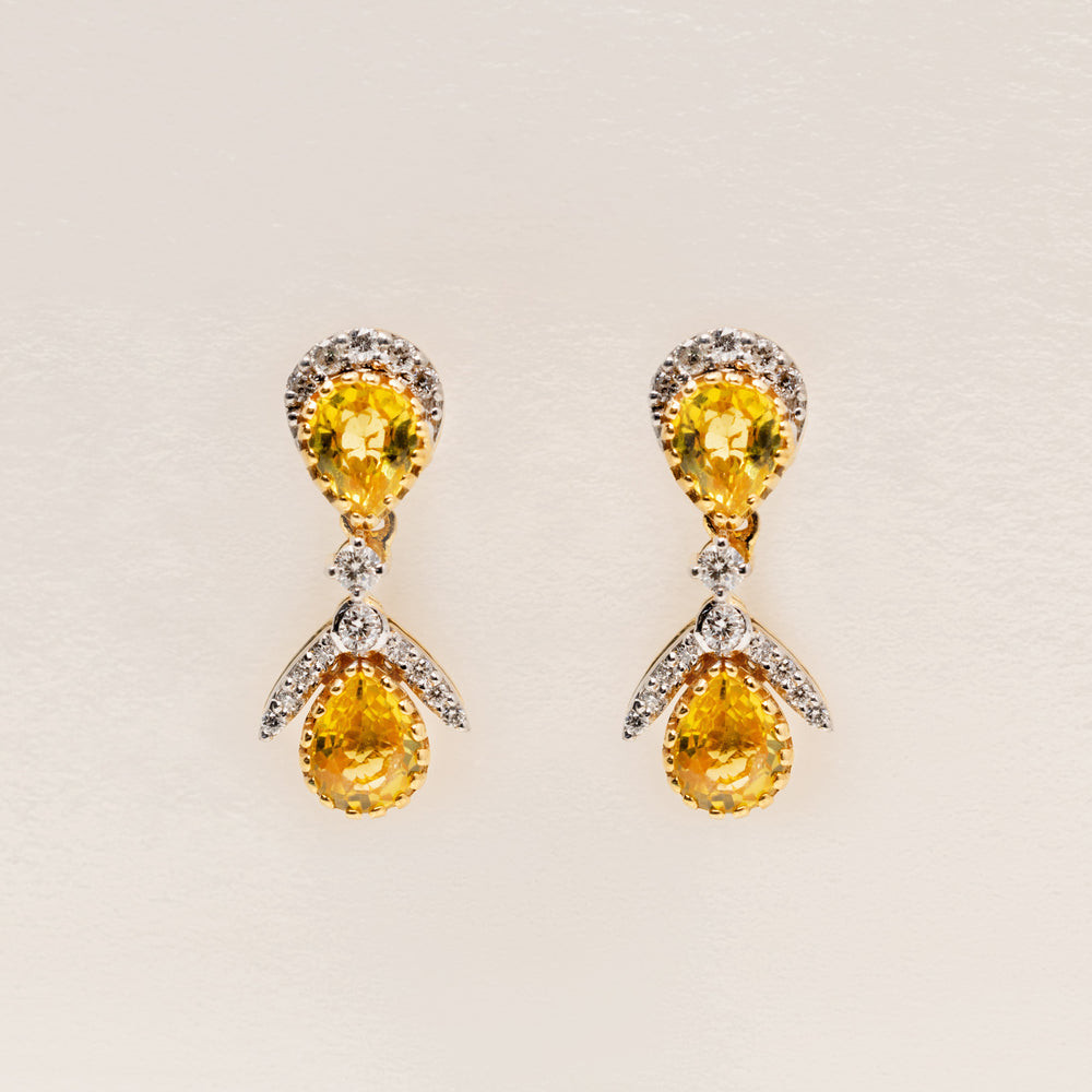 Pair of 18k solid gold earrings with yellow sapphire teardrop gemstone and diamonds on a light beige background