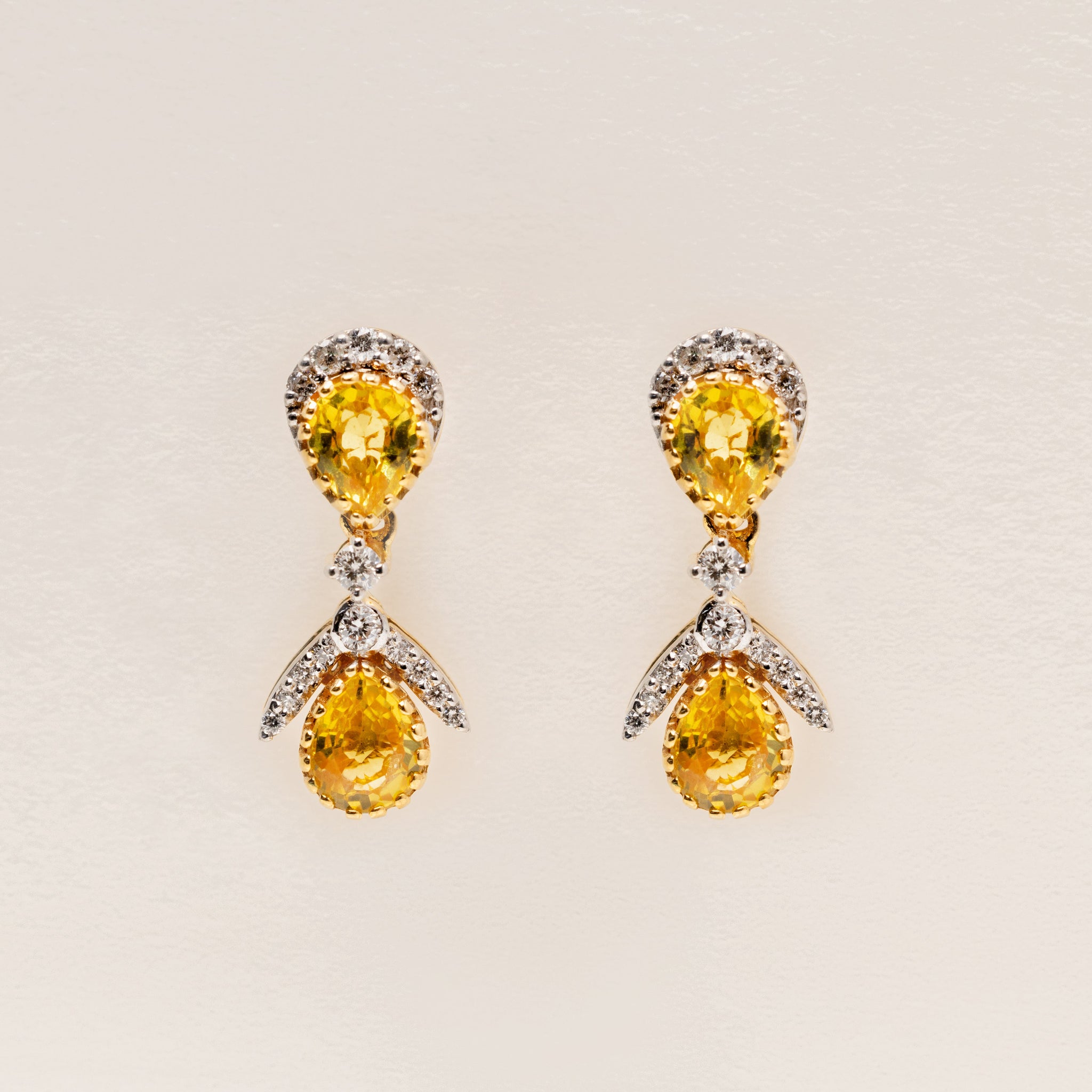 Pair of 18k solid gold earrings with yellow sapphire teardrop gemstone and diamonds on a light beige background