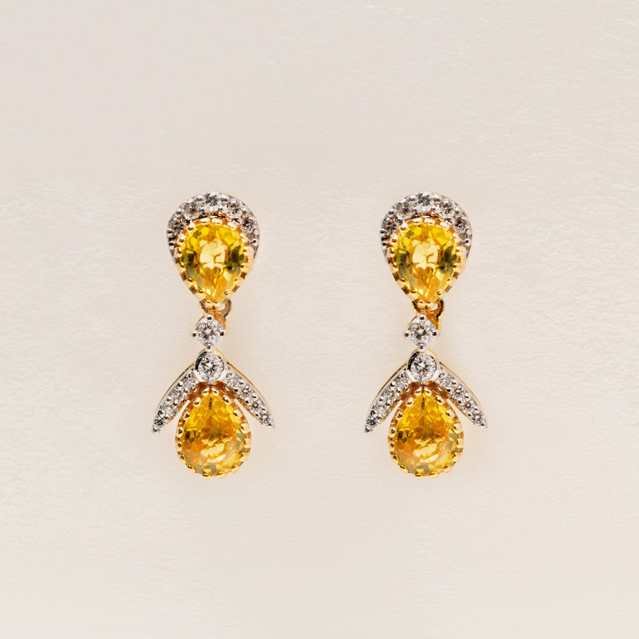 Pair of 18k solid gold earrings with yellow sapphire teardrop gemstone and diamonds on a light beige background