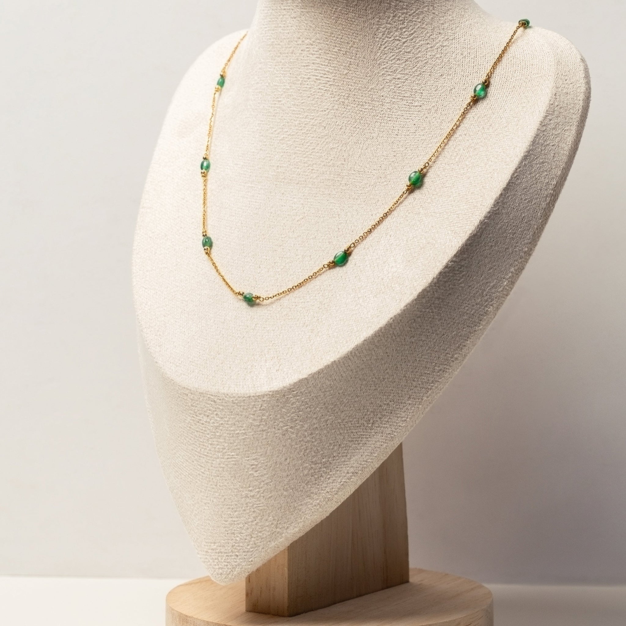 Necklace with green emerald beads like a string of lights on a mannequin bust against a plain background