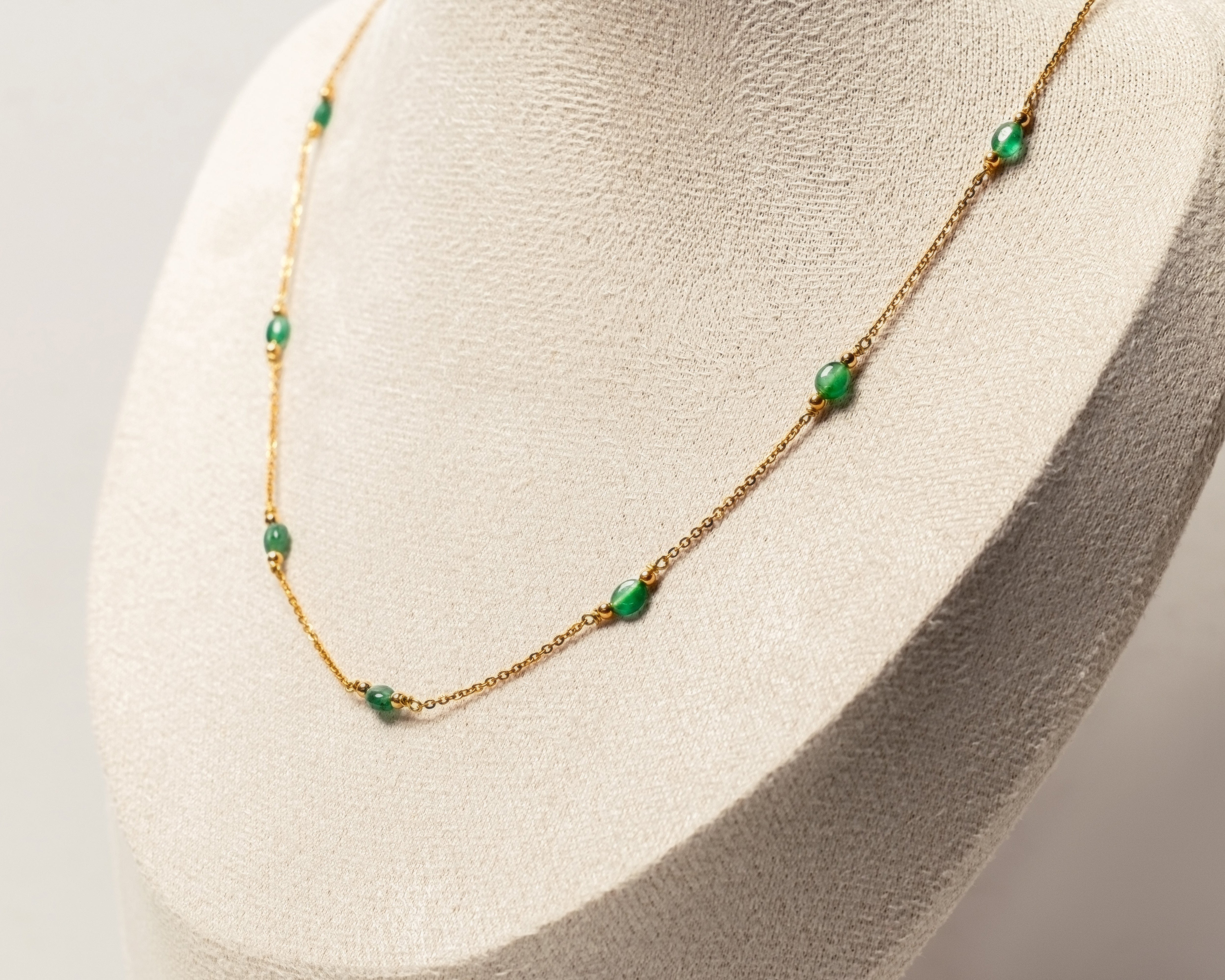 Gold necklace with green emeralds beads on a mannequin head against a neutral background
