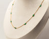 Gold necklace with green emeralds beads on a mannequin head against a neutral background