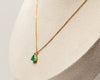 Gold necklace with a green emerald teardrop pendant on a neutral background