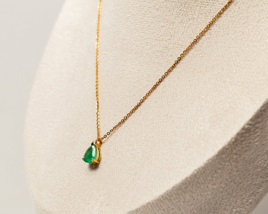 Gold necklace with a green emerald teardrop pendant on a neutral background