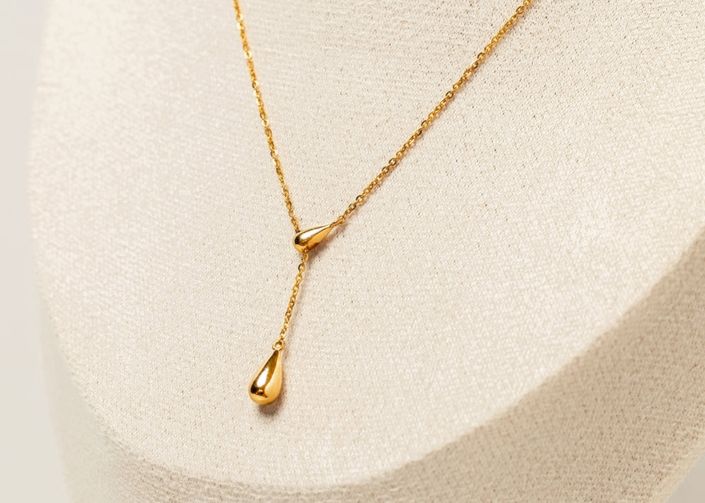 Y shaped Gold necklace with a tear drop pendant on a light beige background