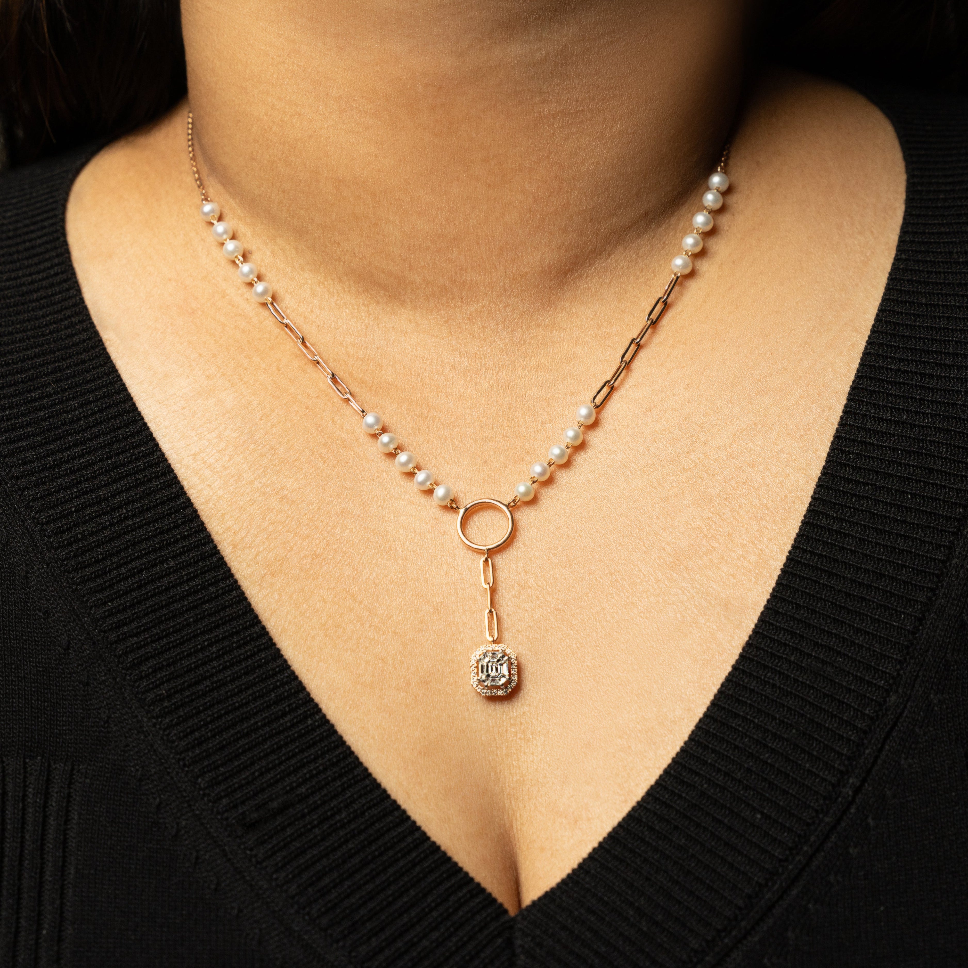 Pearl necklace with a diamond pendant worn by a person in a black top.